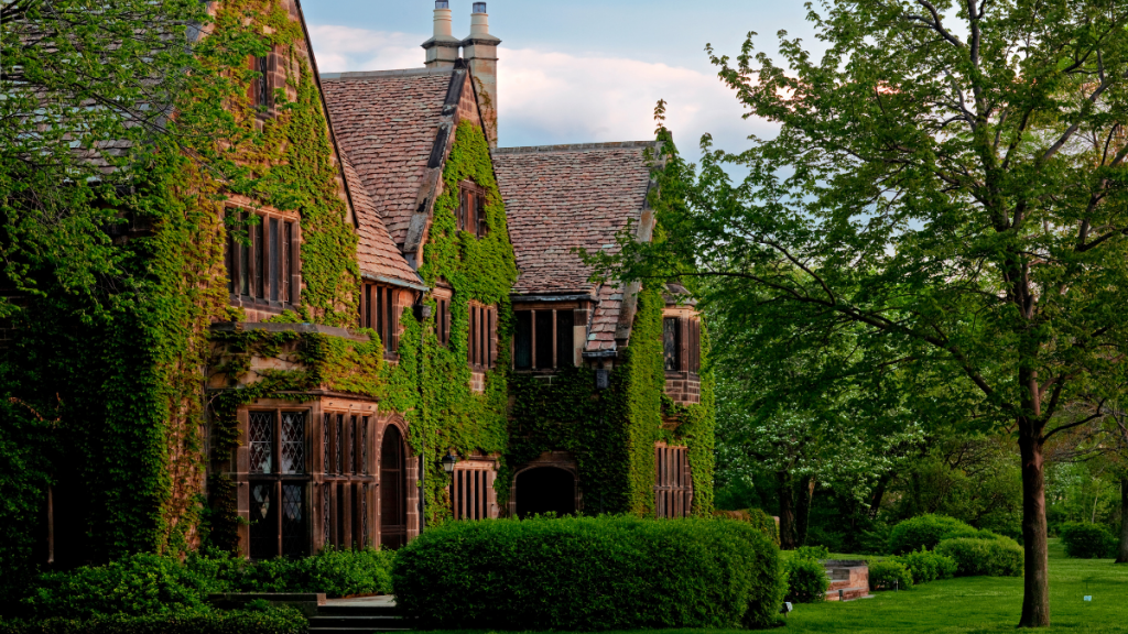 Ivy-covered exterior of the Ford House Main Residence, featuring leaded glass windows, stone and wood detailing, and lush landscaping on a summer afternoon.