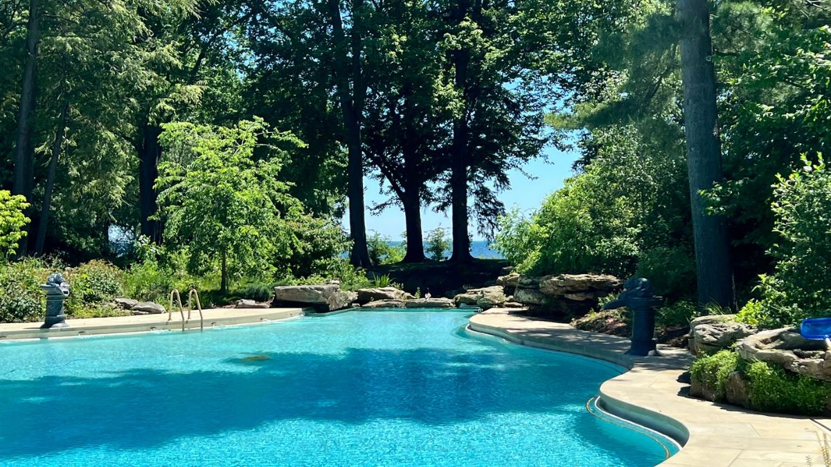 The restored swimming pool at Ford House glistens under bright sunlight, framed by trees and surrounded by lush landscaping.