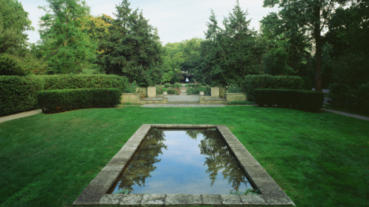 Reflecting pool in the Formal Garden at Ford House, bordered by lush green lawn and symmetrical boxwood hedges, leading to a stone terrace framed by mature trees.
