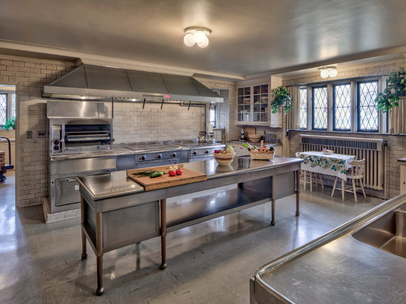 The Main Kitchen at Ford House, featuring stainless steel counters, a large stove with hood, tiled walls.