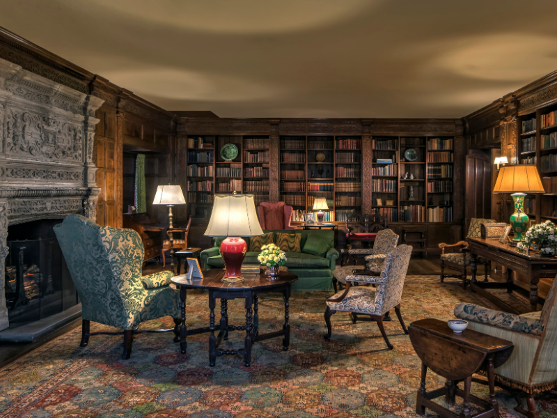 The Library at Ford House, showcasing oak paneling, an ornate stone fireplace, historic books, and classic upholstered furniture."