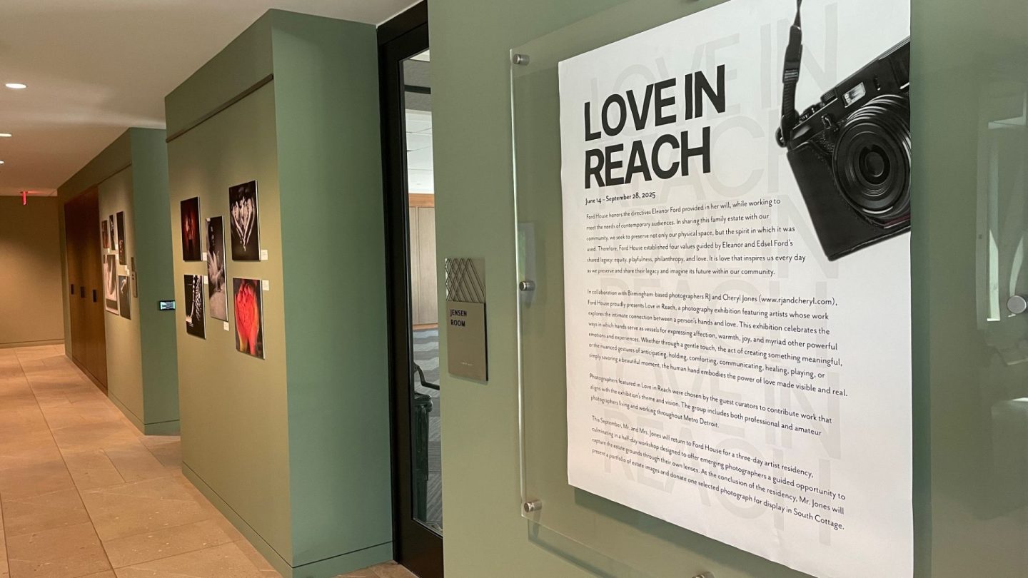 Introductory panel for the “Love in Reach” photography exhibition at Ford House, displayed next to the Jensen Room. The panel features a mounted camera and descriptive text about the exhibit’s themes of love, connection, and touch.