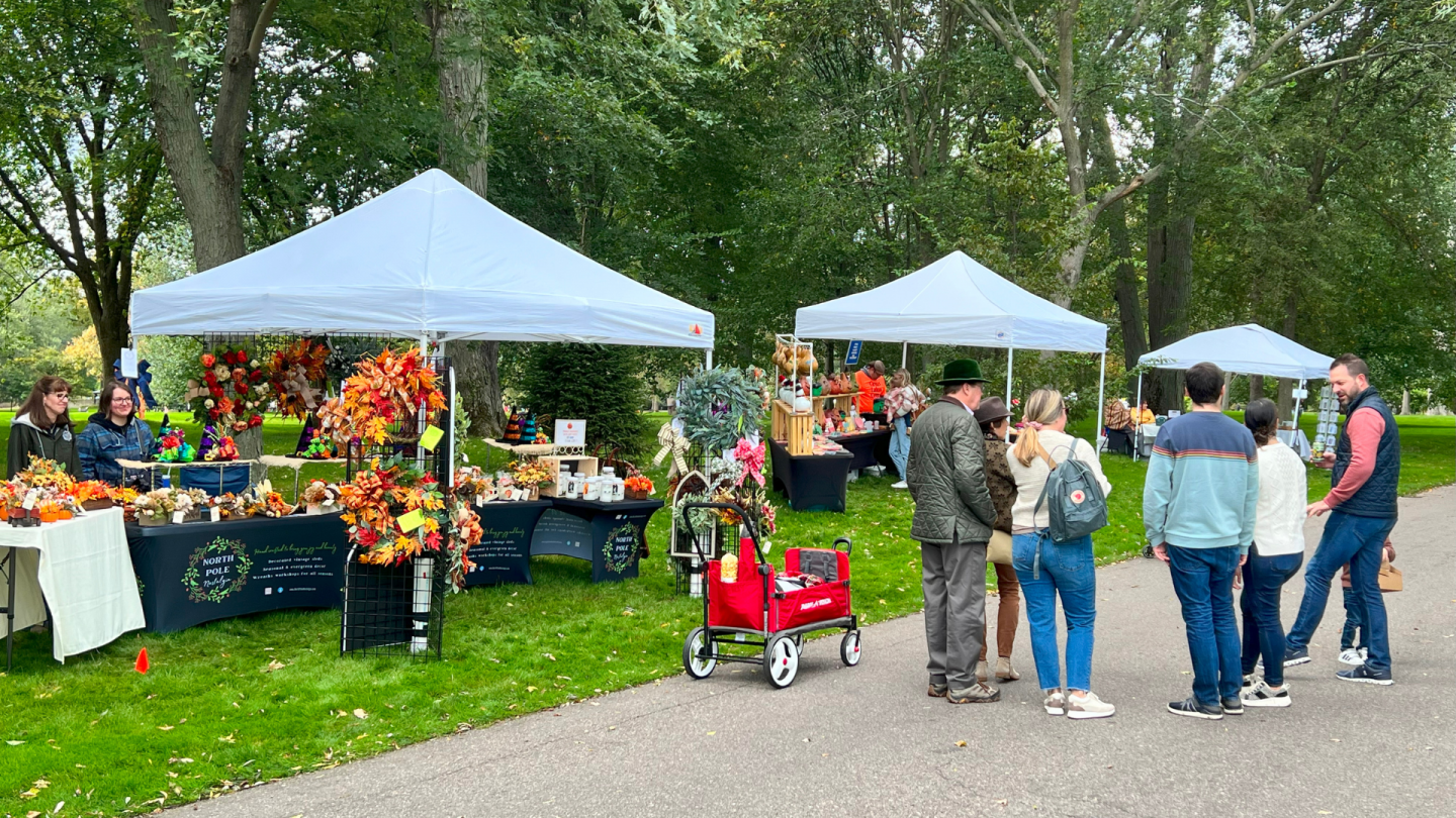 Rows of tents house craft vendors selling fall wreaths, home décor, and festive handmade goods under a canopy of trees.